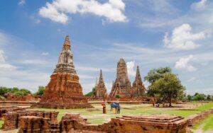 Vue des ruines du temple Wat Chaiwatthanaram à Ayutthaya, Thaïlande, avec ses stupas en briques rouges et son architecture khmère sous un ciel bleu parsemé de nuages