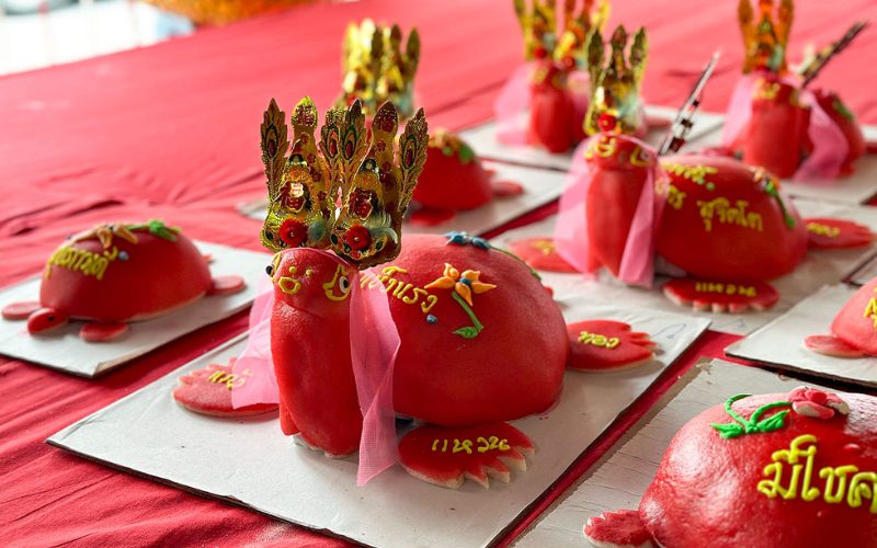 Gâteaux traditionnels rouges en forme de tortue décorés de couronnes dorées et de rubans, exposés sur une table pendant le festival Por Tor à Phuket, symbole d’offrandes aux esprits et aux ancêtres