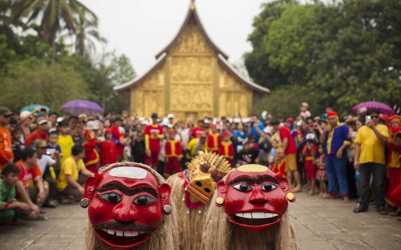Masques traditionnels rouges lors d’une parade du Boun Pi Mai à Luang Prabang, avec une foule rassemblée devant un temple doré pour admirer la performance