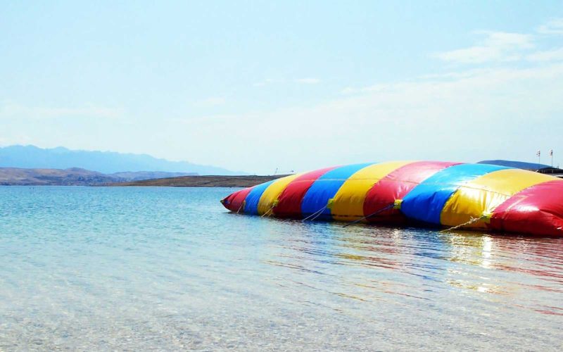 Grand coussin gonflable multicolore flottant sur une eau claire et peu profonde, utilisé pour le jeu de saut "blob jump"