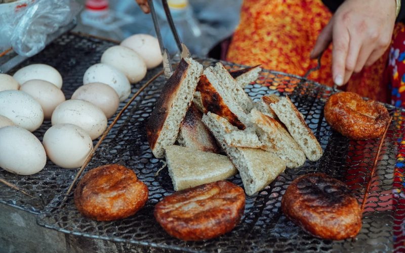 Spécialités de rue de Ha Giang grillées sur un brasero : morceaux de bánh ngô (gâteau de maïs), gâteaux ronds frits et œufs cuits au feu de charbon