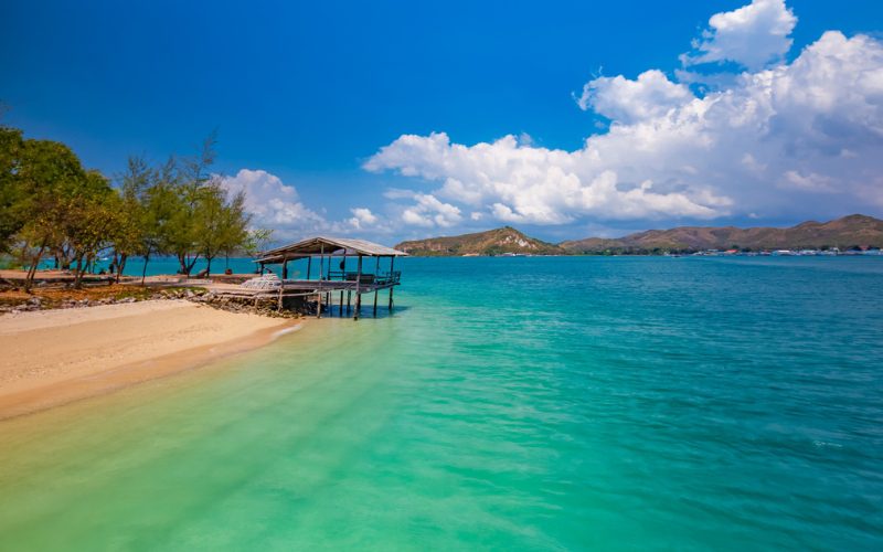 Plage paradisiaque de Koh Larn près de Pattaya, avec sable doré, mer turquoise et cabane en bois sur pilotis face aux collines verdoyantes