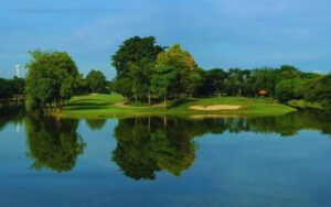 Vue sur un parcours de golf verdoyant entouré d’arbres, avec un plan d’eau calme en premier plan reflétant le paysage