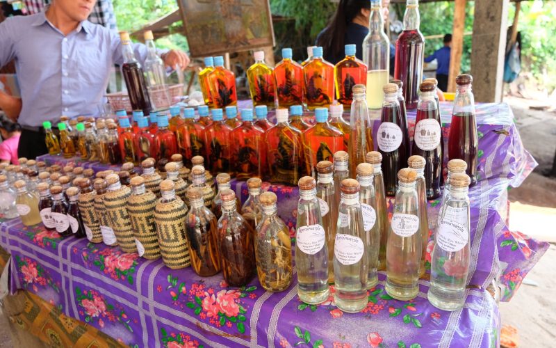 Bouteilles de whisky de riz lao exposées sur un étal de marché à Ban Xang Hai, avec des motifs artisanaux et des bouteilles contenant des ingrédients exotiques