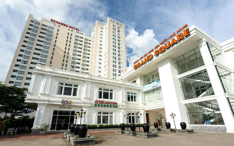 Vue extérieure du complexe hôtelier Becamex Hotel à Binh Duong, avec ses tours modernes, son bâtiment colonial rénové abritant un café et un restaurant, et le centre de conférences Grand Square à la façade vitrée