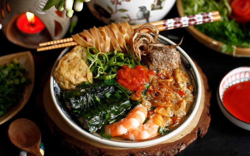 Bol de banh da cua, soupe traditionnelle vietnamienne composée de nouilles de riz, crevettes, viande, tofu frit, feuilles de bétel farcies, tomates, herbes fraîches et garnitures croustillantes, le tout rehaussé d’une sauce rouge parfumée