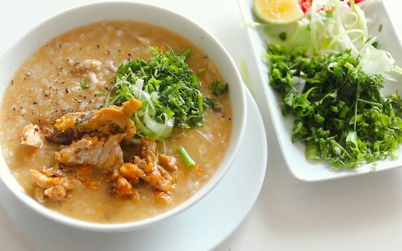 Bol de cháo cá Lăng, bouillie de poisson-chat vietnamienne servie avec herbes fraîches, citron vert et légumes sur le côté