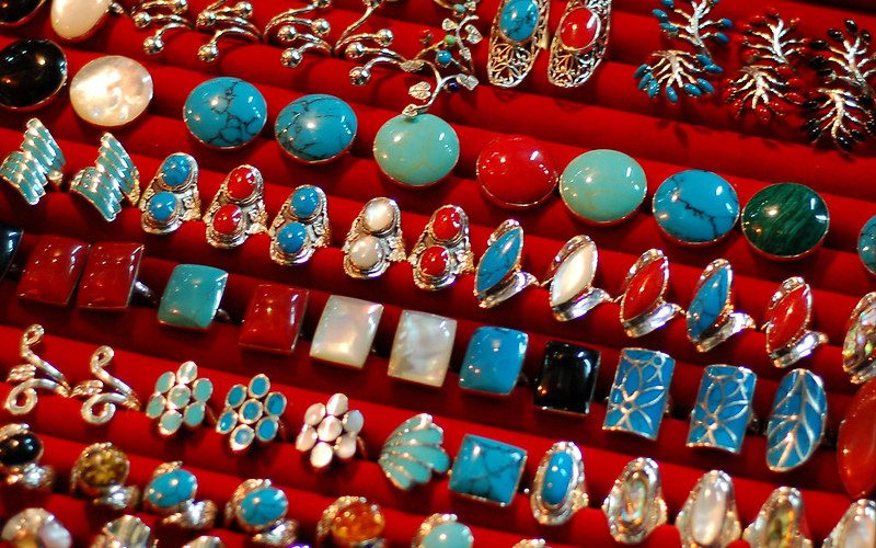 Collection de bijoux thaïlandais en argent sertis de pierres semi-précieuses colorées (turquoise, corail rouge, nacre), soigneusement exposés sur un présentoir rouge