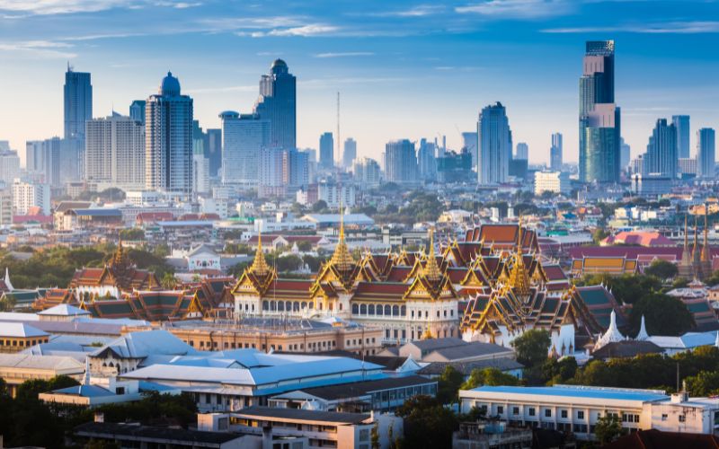 Vue panoramique de Bangkok avec le Grand Palais au premier plan et les gratte-ciel modernes en arrière-plan, symbolisant le contraste entre tradition et modernité