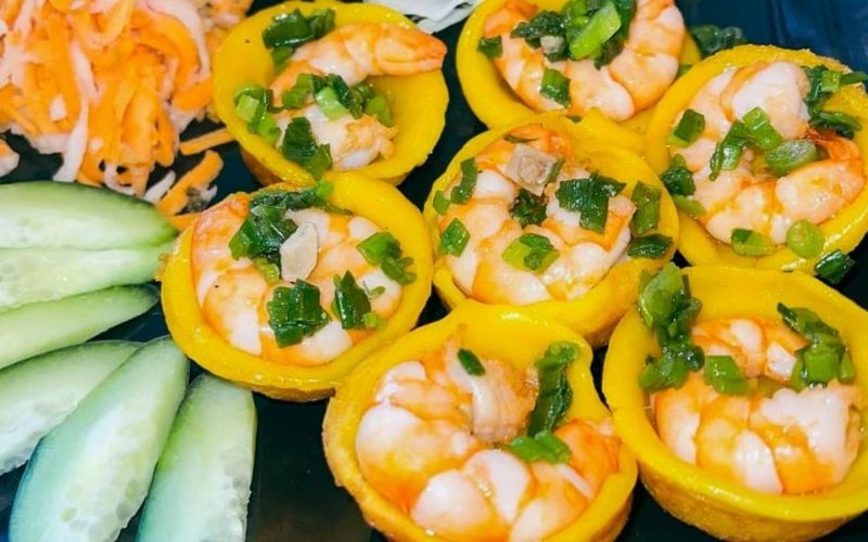 Assortiment de bánh khọt vietnamiens dorés, garnis de crevettes roses et d’oignons verts sautés, accompagnés de tranches de concombre et de légumes marinés