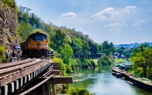 Train traversant le chemin de fer de la mort sur un viaduc en bois au bord de la rivière Kwai, entouré de paysages verdoyants à Kanchanaburi