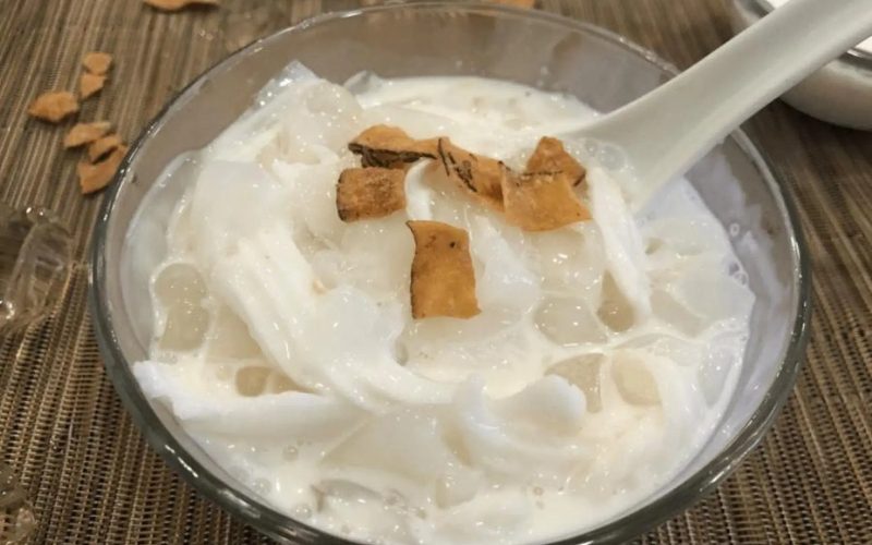 Bol de chè dừa, dessert vietnamien à base de lait de coco onctueux, gelée translucide, lamelles de noix de coco tendre et copeaux grillés, servi frais avec des glaçons pour une saveur douce et rafraîchissante