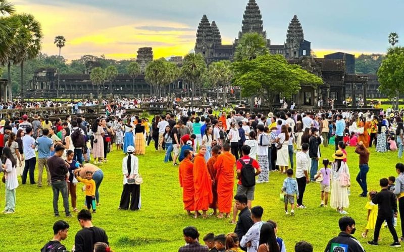Foule de visiteurs et de moines en robe orange rassemblés devant le temple d’Angkor Wat au Cambodge, sous un ciel coloré au coucher du soleil