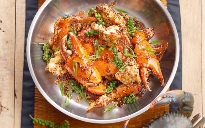 Assiette appétissante de crabe sauté au poivre vert de Kampot, servie dans un bol en métal, avec une sauce épicée brillante, des grains de poivre frais et des herbes aromatiques, plat emblématique de la cuisine cambodgienne côtière