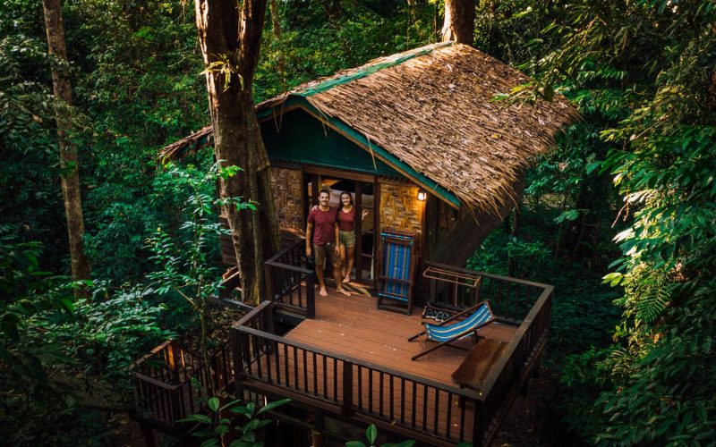 Cabane en bois perchée dans la jungle de Khao Sok, entourée d’une végétation tropicale luxuriante, avec un couple se tenant sur la terrasse d’observation