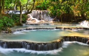 Cascades en terrasses de Kuang Si, avec des bassins d'eau turquoise entourés d'une végétation luxuriante, offrant un paysage naturel apaisant et féerique