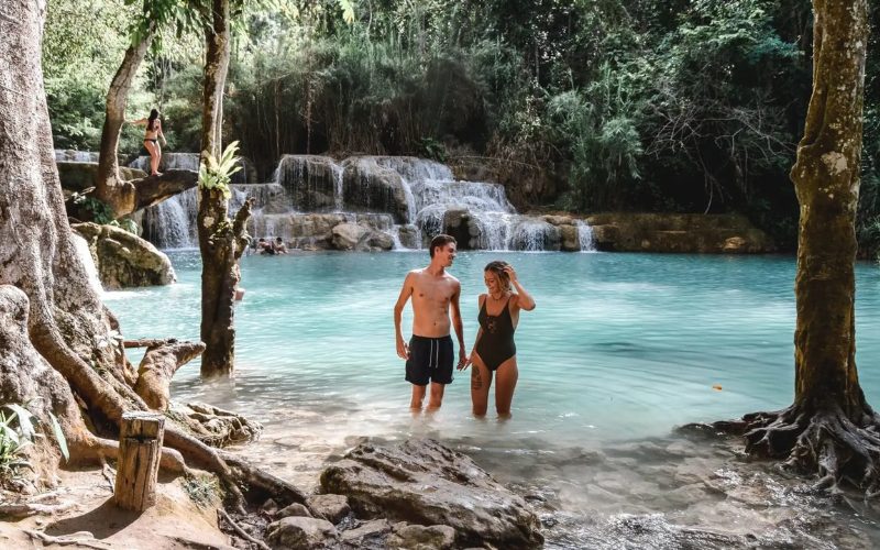 Couple se baignant dans les eaux turquoise des chutes de Kuang Si, entourées de forêt tropicale au Laos