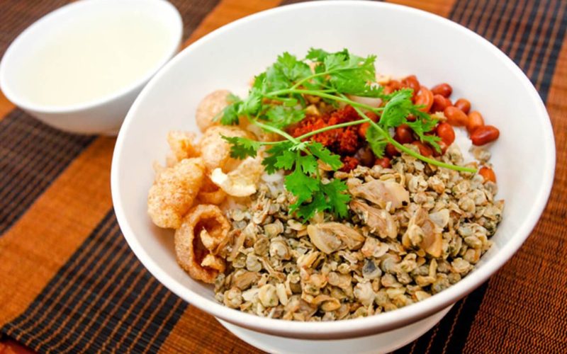 Bol de cơm hến, spécialité de Hué composée de riz blanc, petites palourdes sautées, peau de porc croustillante, cacahuètes grillées, herbes fraîches et piment en poudre