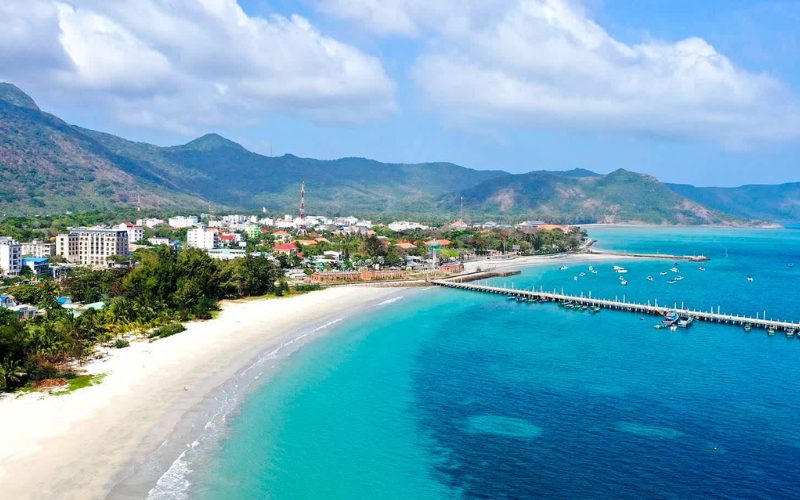 Vue aérienne de la plage de Con Dao, avec sable blanc, mer turquoise, jetée et montagnes verdoyantes, destination paisible et romantique du Vietnam