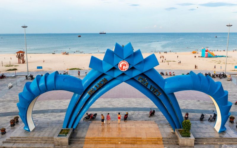 Portail bleu emblématique de la plage de Cua Viet à Quang Tri, avec vue sur le sable blanc, la mer et les vacanciers en arrière-plan