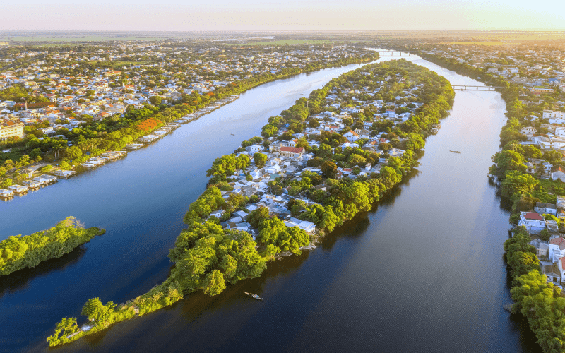 Vue aérienne de l'île Cồn Hến au milieu de la rivière des Parfums à Hué, Vietnam, entourée de maisons traditionnelles et de verdure luxuriante.