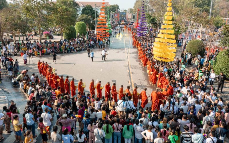 Grand défilé de moines bouddhistes vêtus de robes safran avançant entre deux rangées de fidèles lors d’une procession du Nouvel An khmer, au milieu de décorations colorées suspendues dans la rue