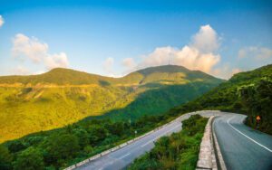 Route sinueuse du col de Hai Van au Vietnam, traversant des montagnes verdoyantes sous un ciel bleu avec quelques nuages