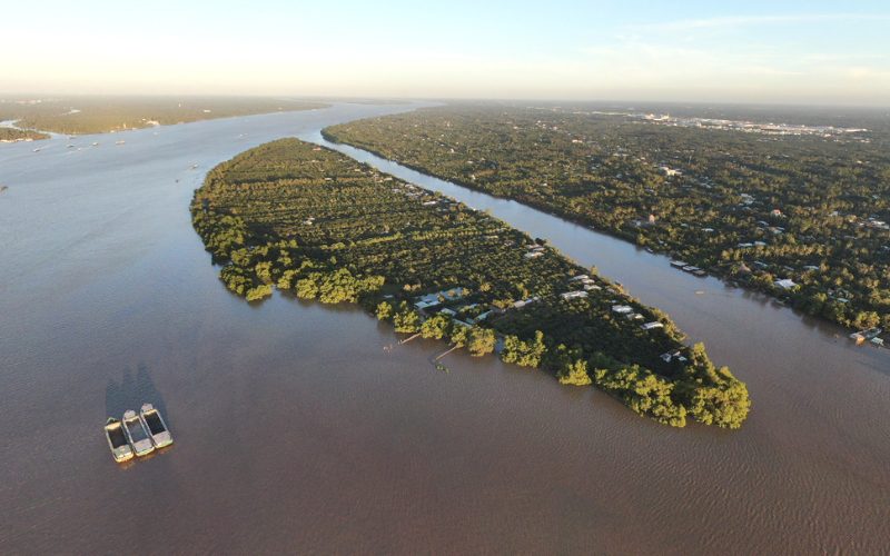 Vue aérienne d’un îlot verdoyant à Vinh Long, entouré par les larges bras du Mékong, avec des vergers, habitations rurales et bateaux naviguant sur le fleuve