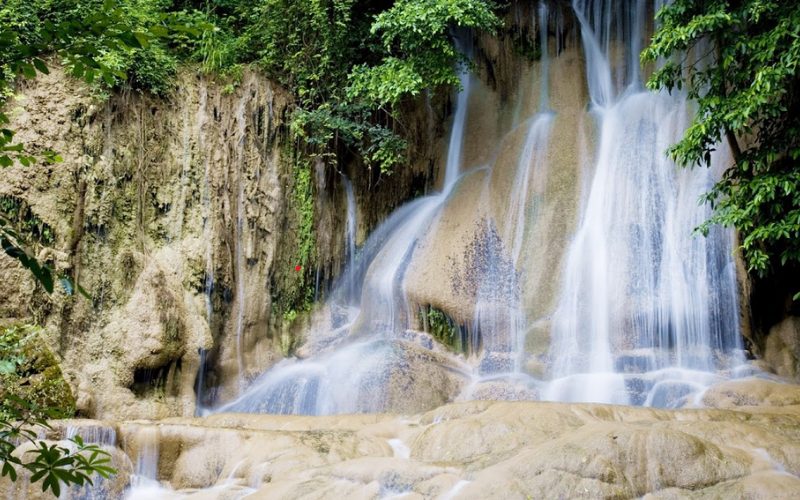 Cascade entourée de végétation luxuriante, avec des eaux cristallines s'écoulant en douceur sur des rochers calcaires