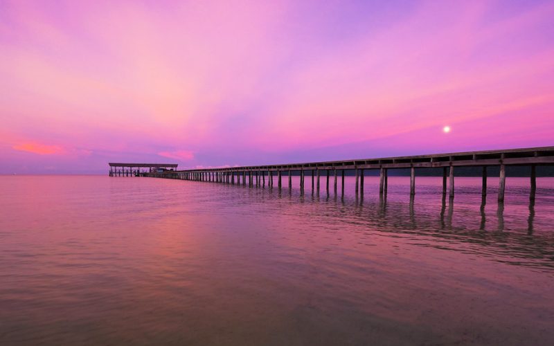 Long ponton en bois s’avançant sur la mer au coucher du soleil, sous un ciel rose et violet spectaculaire à Koh Rong Samloem