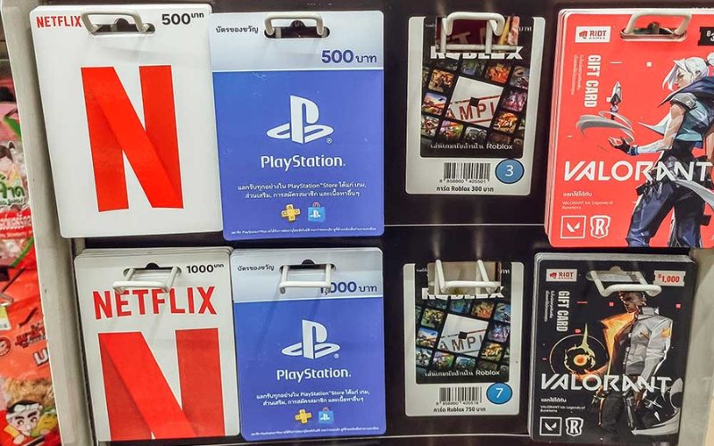 Présentoir de cartes cadeaux dans un 7-Eleven en Thaïlande, incluant Netflix, PlayStation Store, Roblox et Valorant