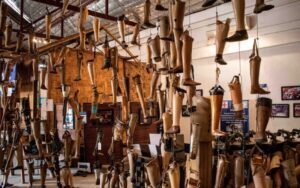 Salle d’exposition remplie de prothèses en bois suspendues, dans un centre de réhabilitation pour victimes de mines au Laos, illustrant l’impact des conflits passés et les efforts de soutien humanitaire