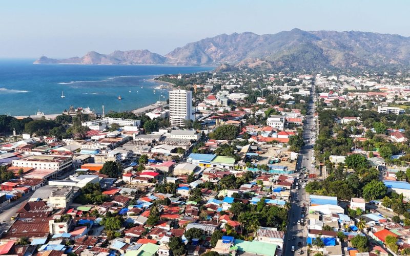 Vue aérienne de Dili, capitale du Timor oriental, avec la ville côtière, la mer bleue, les collines montagneuses et les quartiers urbains en bord de littoral