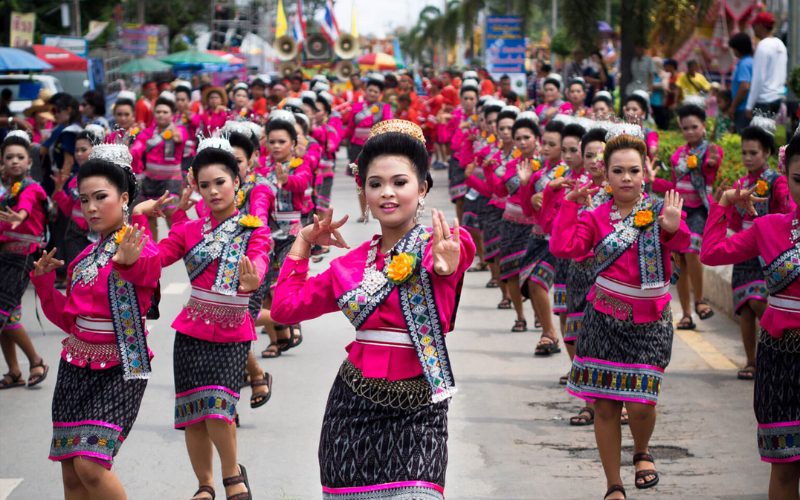 Danseuses en costume traditionnel rose vif défilant en formation lors de la fête des fusées Bun Bang Fai, exécutant des mouvements synchronisés au milieu d'une rue animée