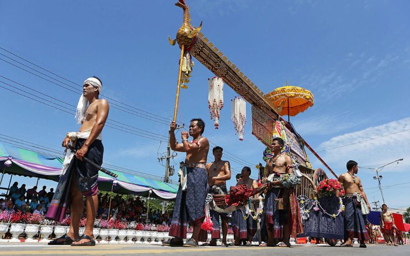 Défilé traditionnel pendant la fête des fusées Bun Bang Fai, avec des hommes torse nu en tenue traditionnelle portant une grande fusée décorée