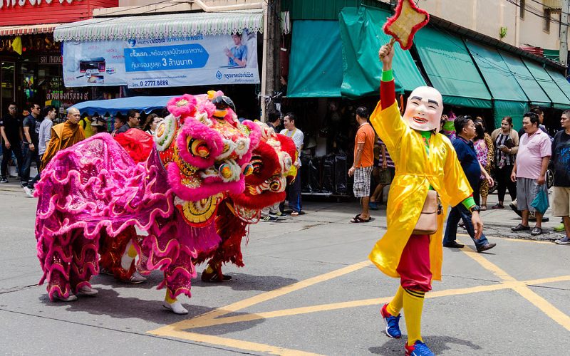 Danse du lion colorée dans les rues de Phuket pendant le festival Por Tor, avec un interprète en costume traditionnel et masque souriant menant le défilé devant une foule de spectateurs