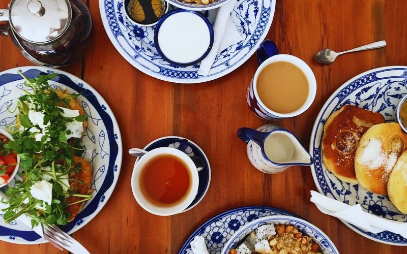 Petit-déjeuner appétissant servi sur des assiettes en céramique décorée de style traditionnel : pain sucré, muesli avec fruits tropicaux, galettes de légumes avec herbes fraîches, thé, café et lait