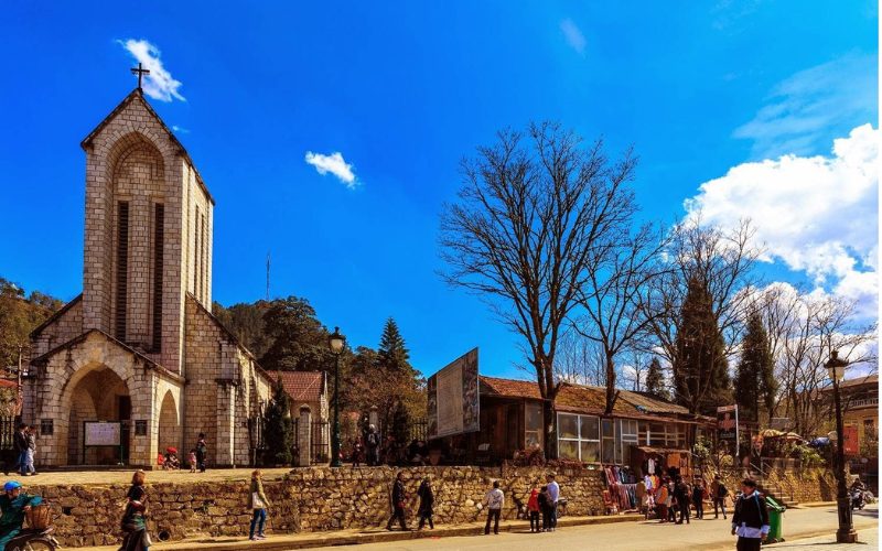 Église de pierre de Sapa au Vietnam, monument emblématique de style gothique niché au cœur de la ville, entourée de visiteurs et de petites échoppes locales sous un ciel bleu éclatant