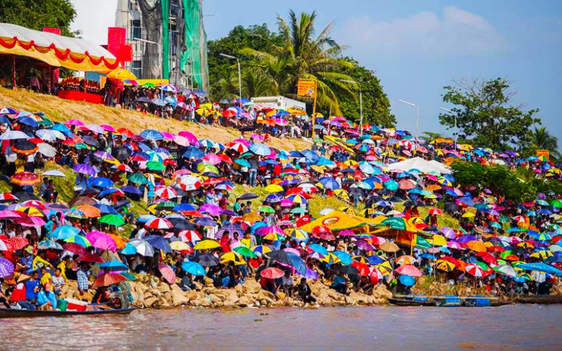 Foule dense rassemblée sur les rives du Mékong lors de la Fête des pirogues Boun Suang Heua au Laos, protégée du soleil par une multitude de parapluies colorés, créant un paysage vibrant et animé