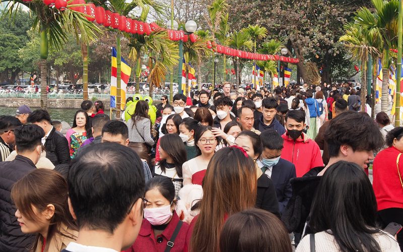 Foule dense de personnes se promenant sur une allée décorée de lanternes rouges et de drapeaux colorés à Hanoï pendant les célébrations du Nouvel An lunaire