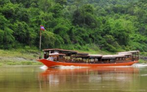 Bateau traditionnel naviguant sur le fleuve Mékong, entouré de collines verdoyantes et d'une végétation luxuriante