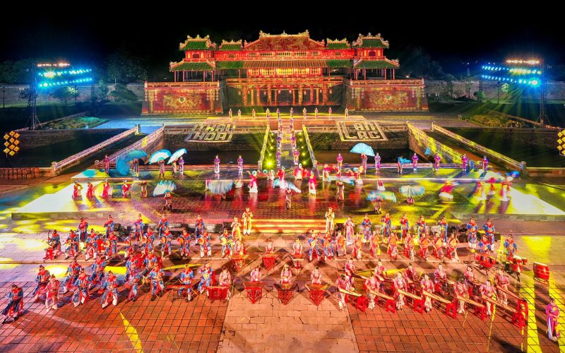 Spectacle nocturne du Festival de Huê devant la Cité impériale, avec danseurs en costumes traditionnels, musiciens et jeux de lumières colorés mettant en valeur l’architecture royale vietnamienne