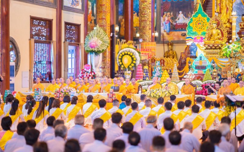 Cérémonie de la fête de Vu Lan dans une pagode au Vietnam, avec des moines en robe safran et des fidèles vêtus de blanc et d’écharpes jaunes, priant ensemble dans un cadre richement décoré