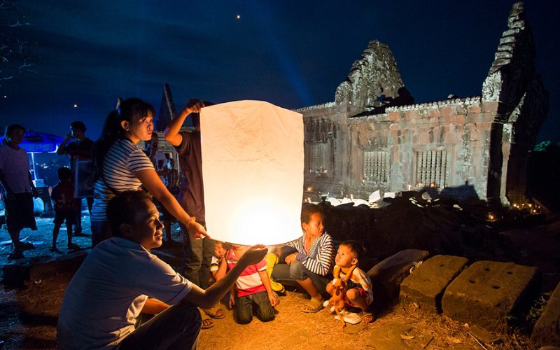Famille laotienne lançant une lanterne céleste lors du Boun Wat Phou, illuminant les ruines sacrées de nuit