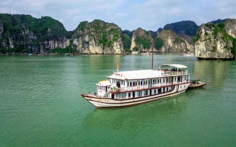 Bateau de croisière naviguant sur les eaux émeraude de la baie d’Halong, entouré de formations karstiques majestueuses et verdoyantes