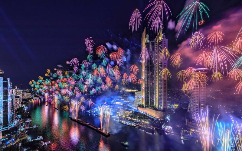Grand feu d’artifice multicolore illuminant la rivière Chao Phraya et les gratte-ciel de Bangkok, avec des reflets éclatants sur l’eau et une ambiance festive spectaculaire autour d’ICONSIAM