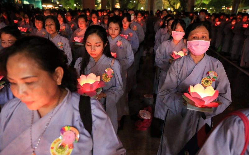 Des femmes vietnamiennes en tunique traditionnelle participent à une cérémonie de la fête des fantômes, tenant chacune une lanterne en forme de fleur de lotus allumée, symbole de paix et de recueillement