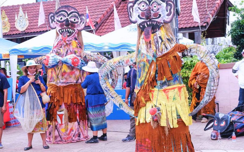 Effigies géantes aux visages grotesques et bras démesurés exposées dans la rue lors du festival Phi Ta Khon à Dan Sai, entourées de villageois en tenue traditionnelle
