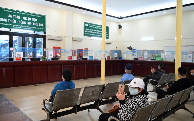 Salle d’attente d’une gare au Vietnam avec des voyageurs assis devant les guichets de vente de billets, dans une ambiance calme et ordonnée