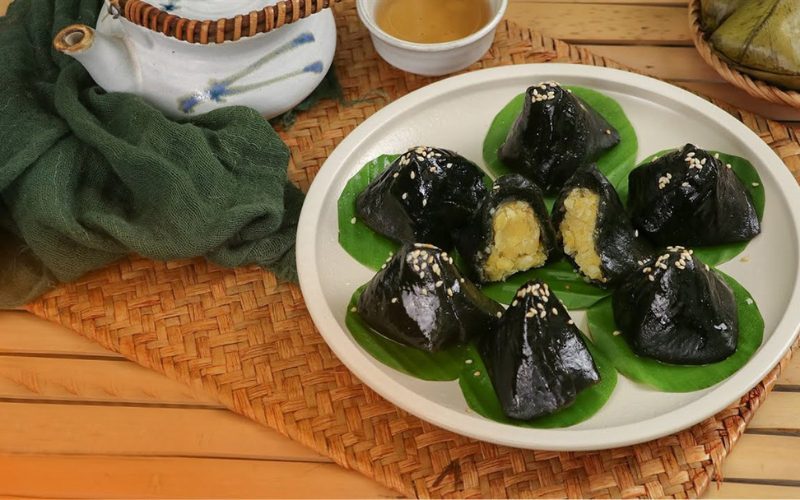 Assiette de bánh ít lá gai, gâteaux vietnamiens noirs à base de feuilles de gai farcis aux haricots mungo sucrés, décorés de graines de sésame